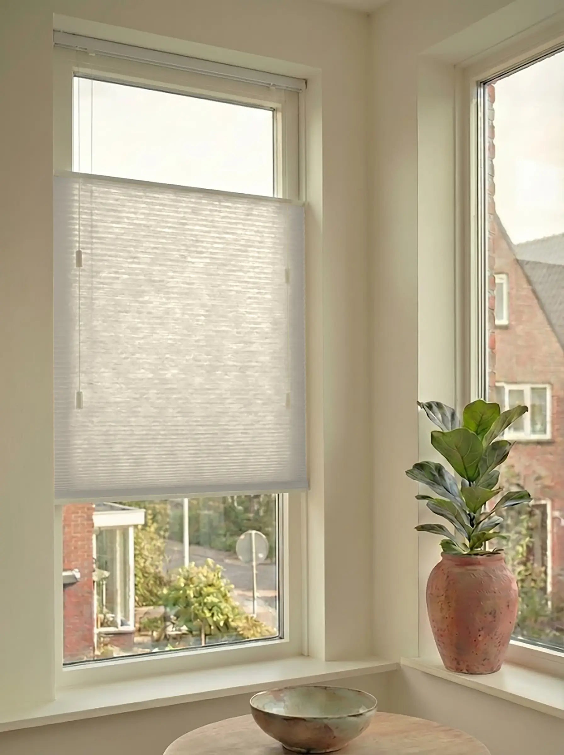 Lichtdoorlatend plisségordijn in Top Down Bottom Up uitvoering, gemonteerd in een licht interieur bij een raam met uitzicht.