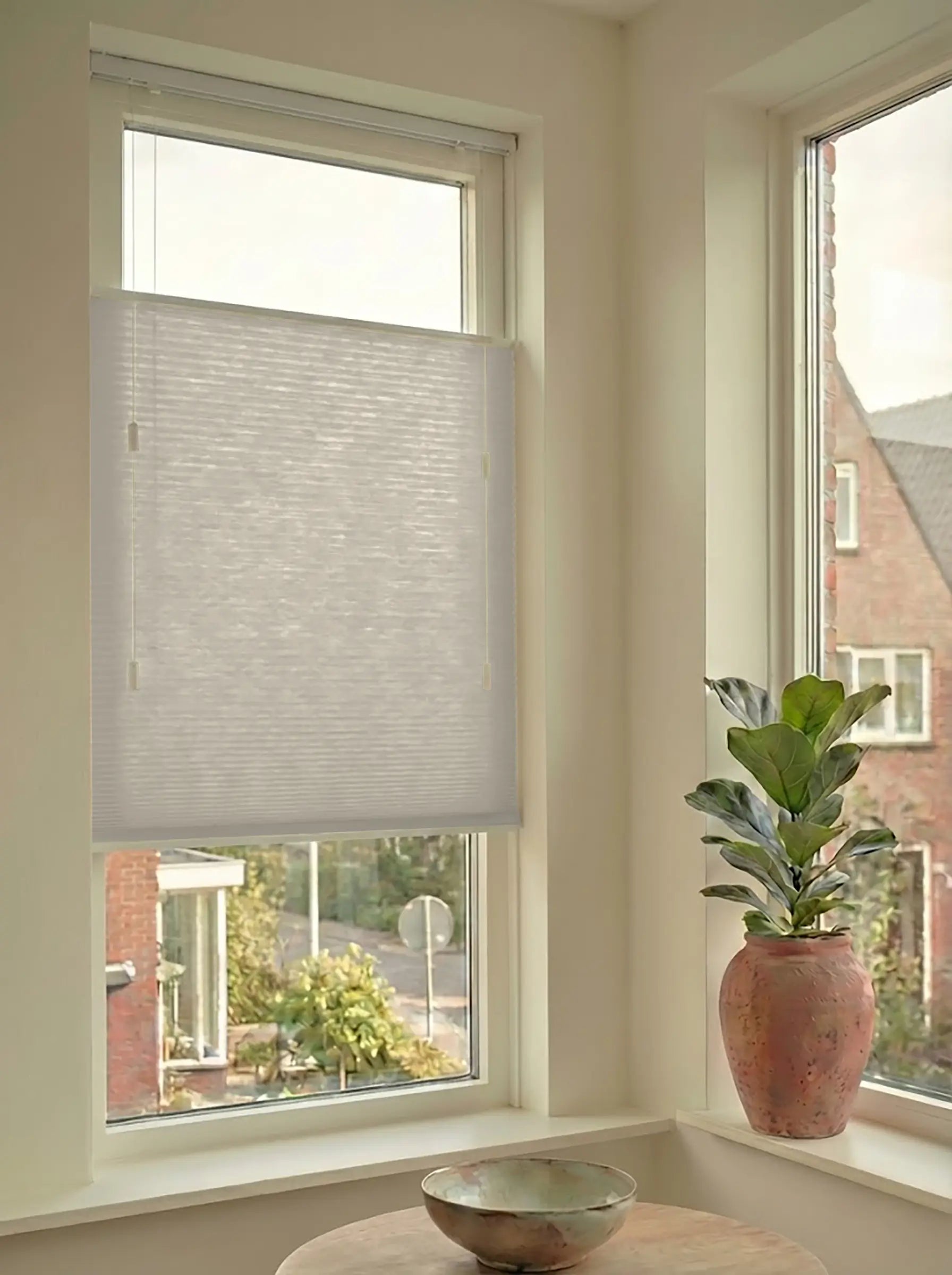 Lichtdoorlatend plisségordijn in Top Down Bottom Up uitvoering, gemonteerd in een licht interieur bij een raam met uitzicht.