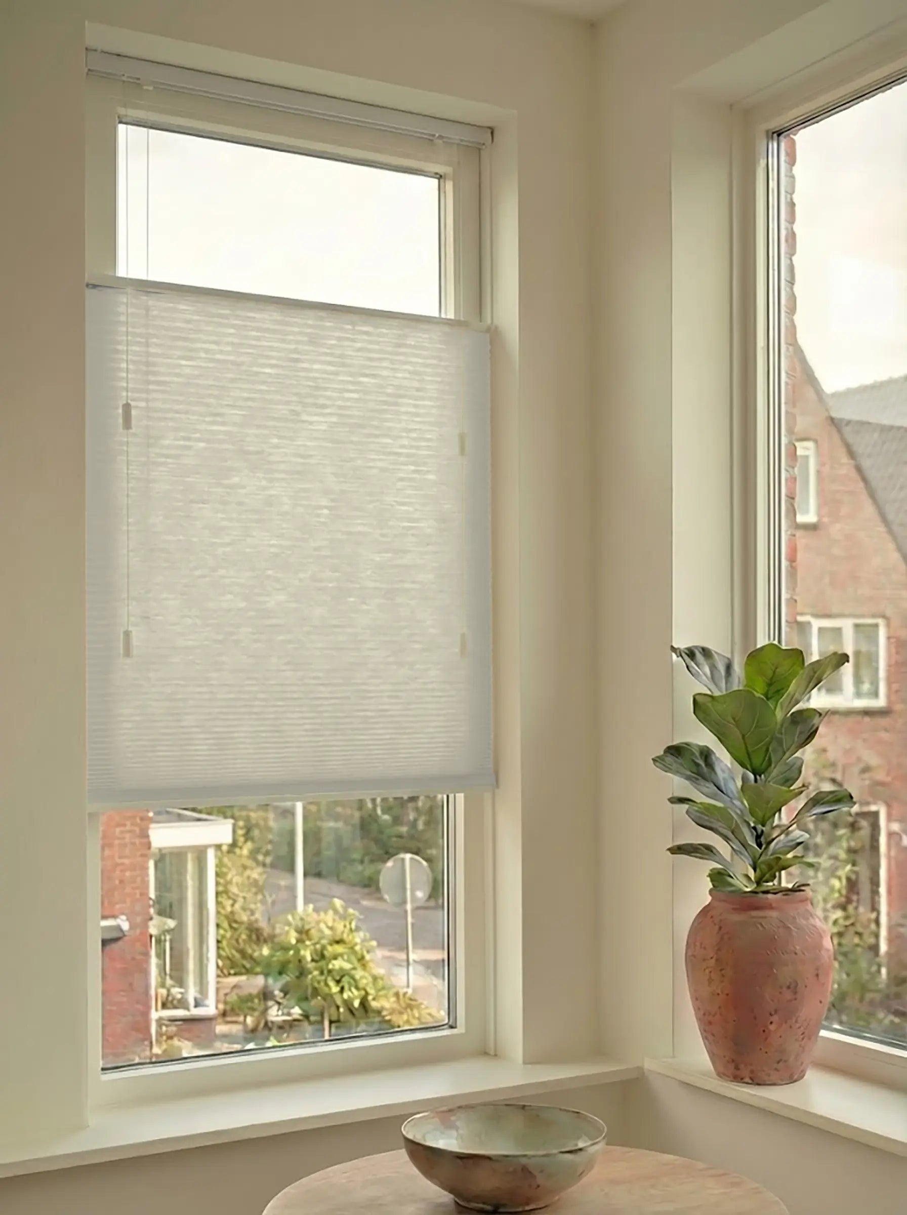 Lichtdoorlatend plisségordijn in Top Down Bottom Up uitvoering, gemonteerd in een licht interieur bij een raam met uitzicht.